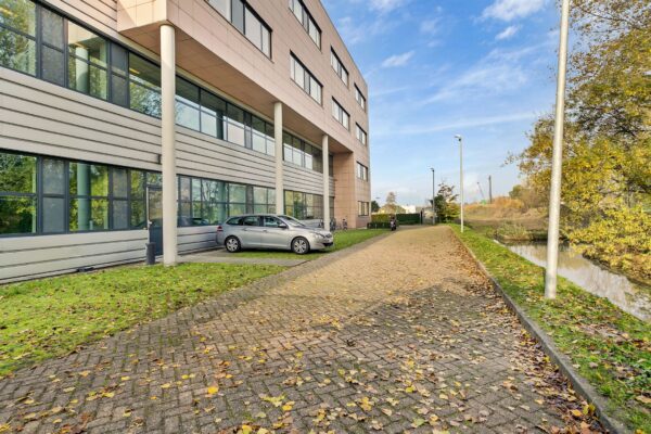 Een modern kantoorgebouw aan de Laan van ‘s-Gravenmade met geparkeerde auto’s en een rustige weg langs een waterpartij.