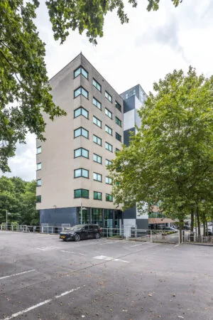 Kantoorgebouw aan de Daltonlaan met parkeerplaats op de voorgrond, omgeven door bomen.