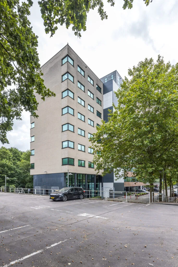 Kantoorgebouw aan de Daltonlaan met parkeerplaats op de voorgrond, omgeven door bomen.