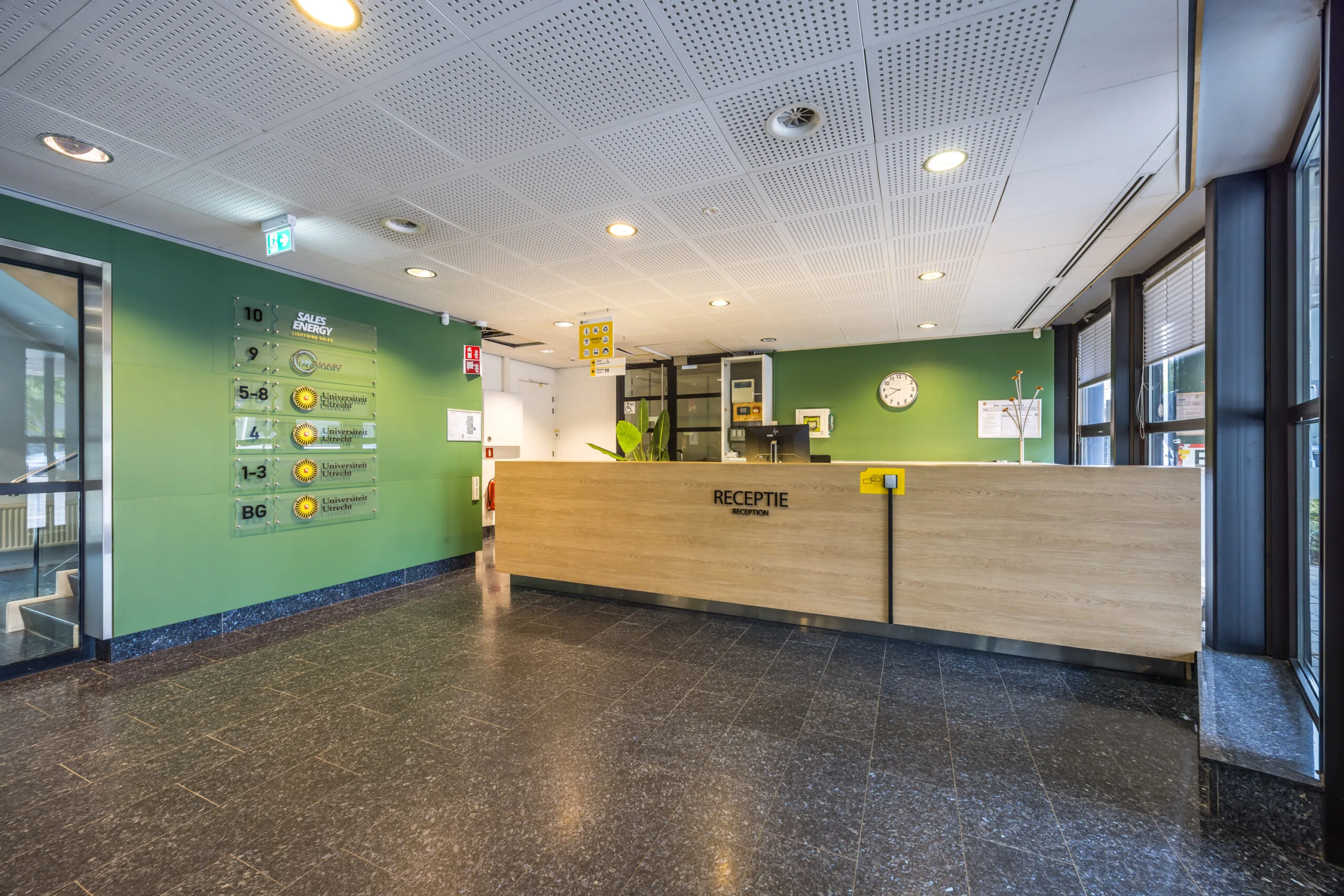 Receptiebalie in de centrale hal van het kantoorgebouw aan de Daltonlaan, met aanduidingen van verschillende verdiepingen en organisaties.