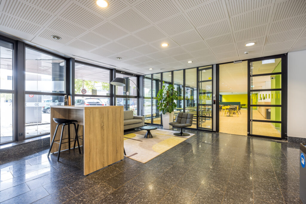 Moderne en lichte ontvangstruimte in het kantoorpand aan de Daltonlaan, met zitgedeelte, hoge tafel en doorkijk naar vergaderruimte.