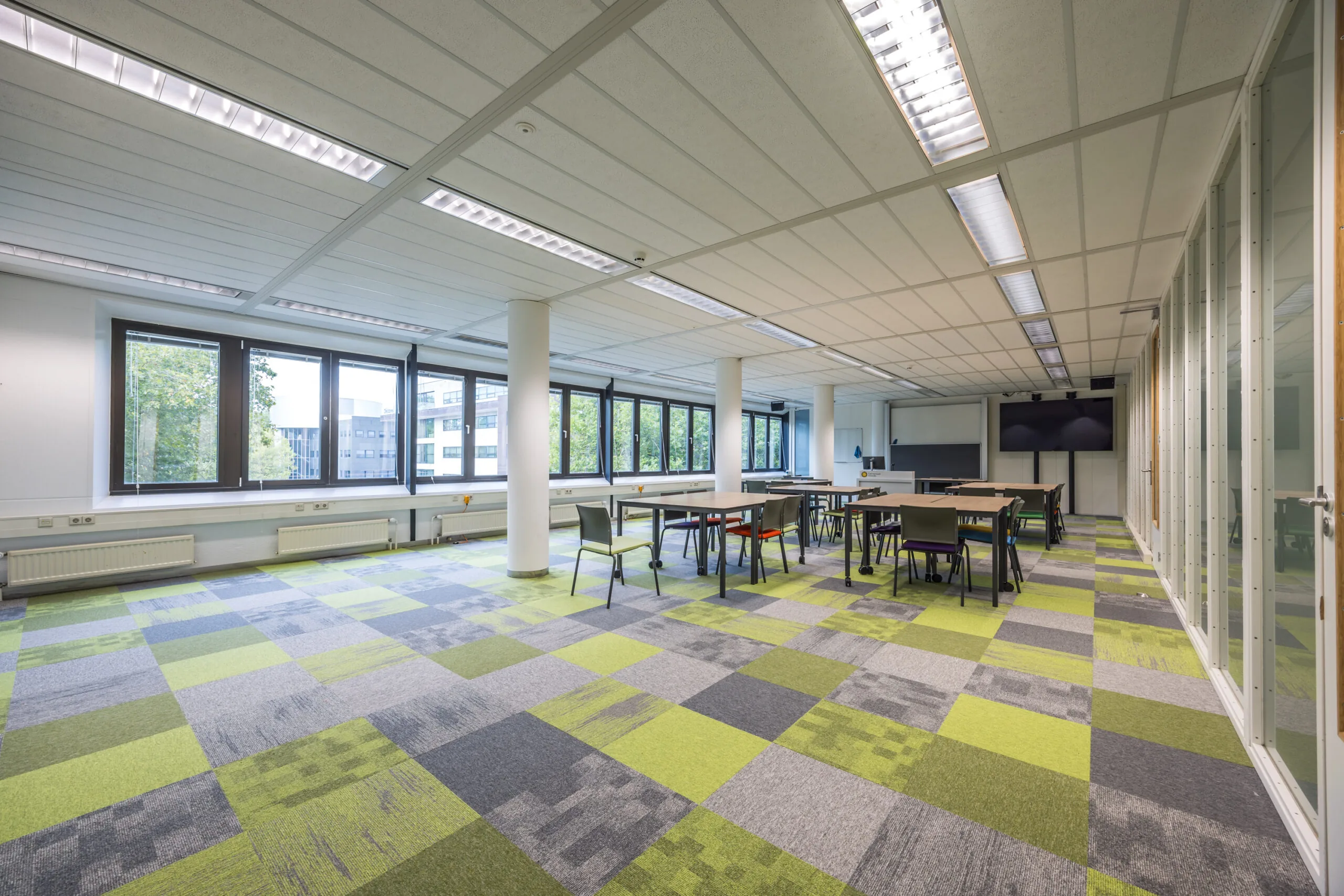 Moderne kantoorruimte aan de Daltonlaan met kleurrijke vloerbedekking, grote ramen en flexibele werkplekken.