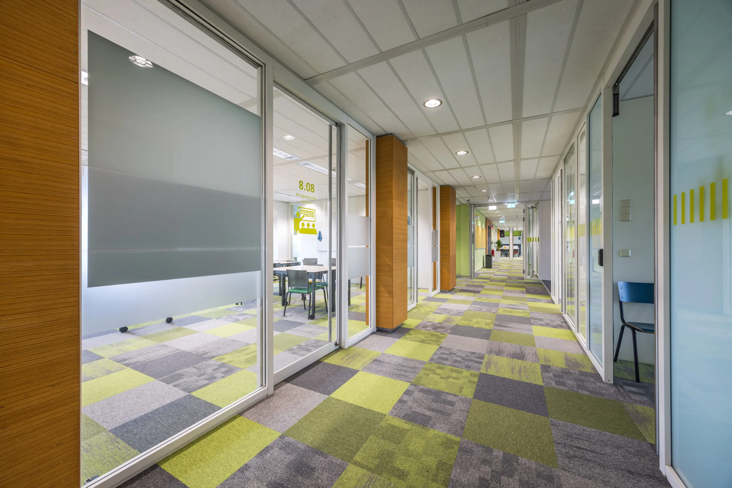 Moderne kantoor- of schoolgang aan de Daltonlaan met glazen wanden en groen-grijs geblokt tapijt.