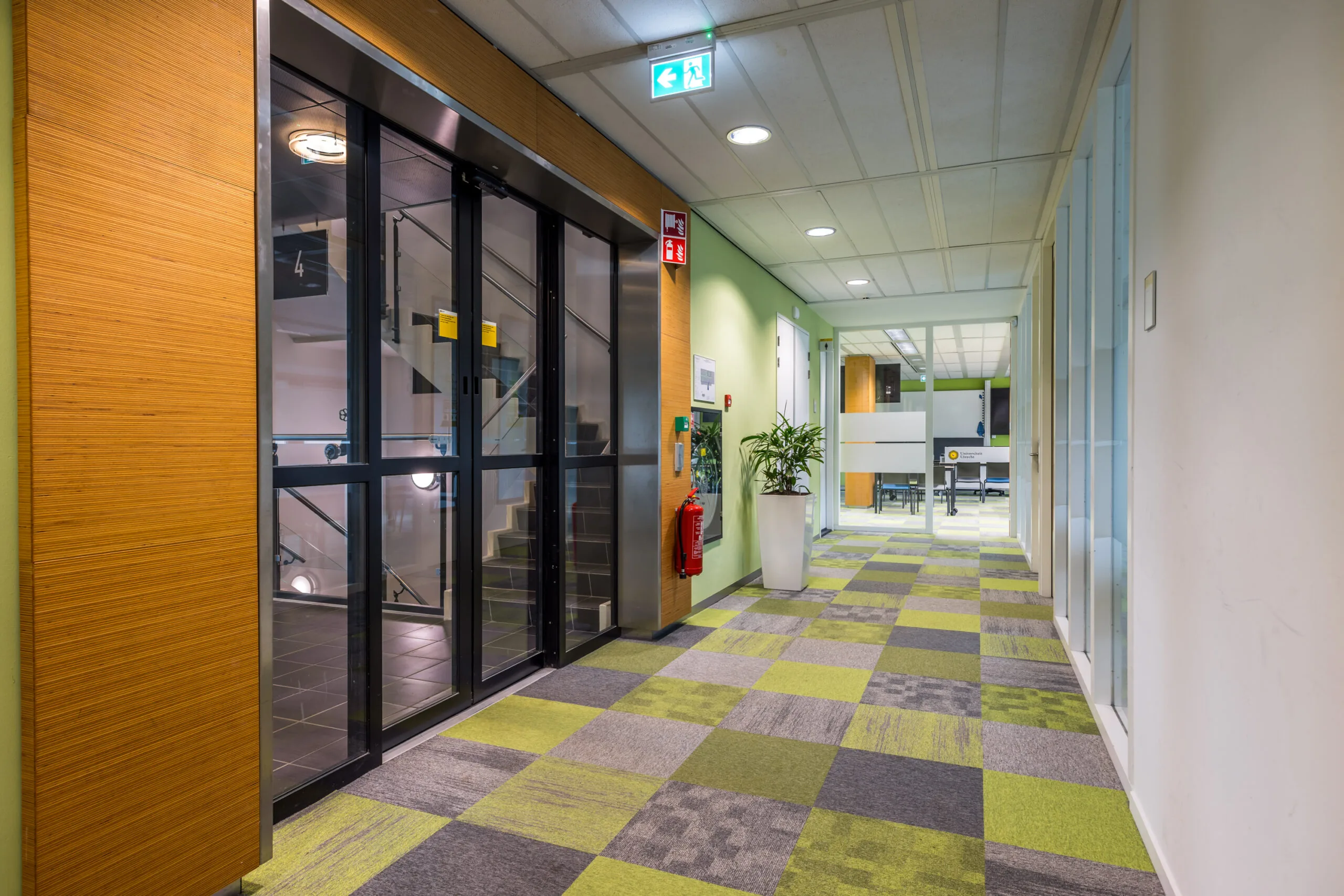 Moderne kantoorhal in het kantoorgebouw aan de Daltonlaan met gekleurde tapijttegels, glazen deuren en een trapopgang.