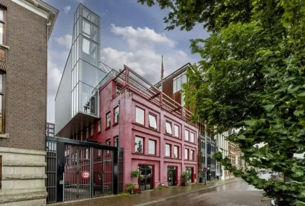 Modern glazen gebouw bovenop een klassiek rood bakstenen pand aan de De Ruijterkade in Amsterdam.