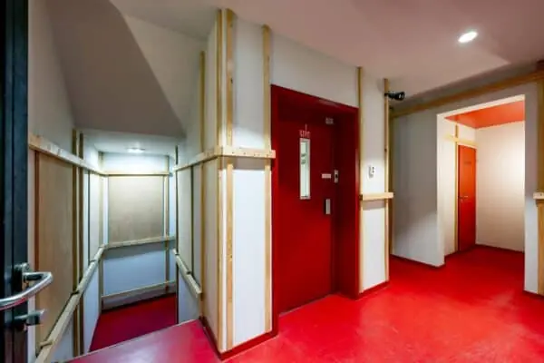 Hal met rode vloer en deuren, inclusief lift en trap, in een gebouw aan de De Ruijterkade.