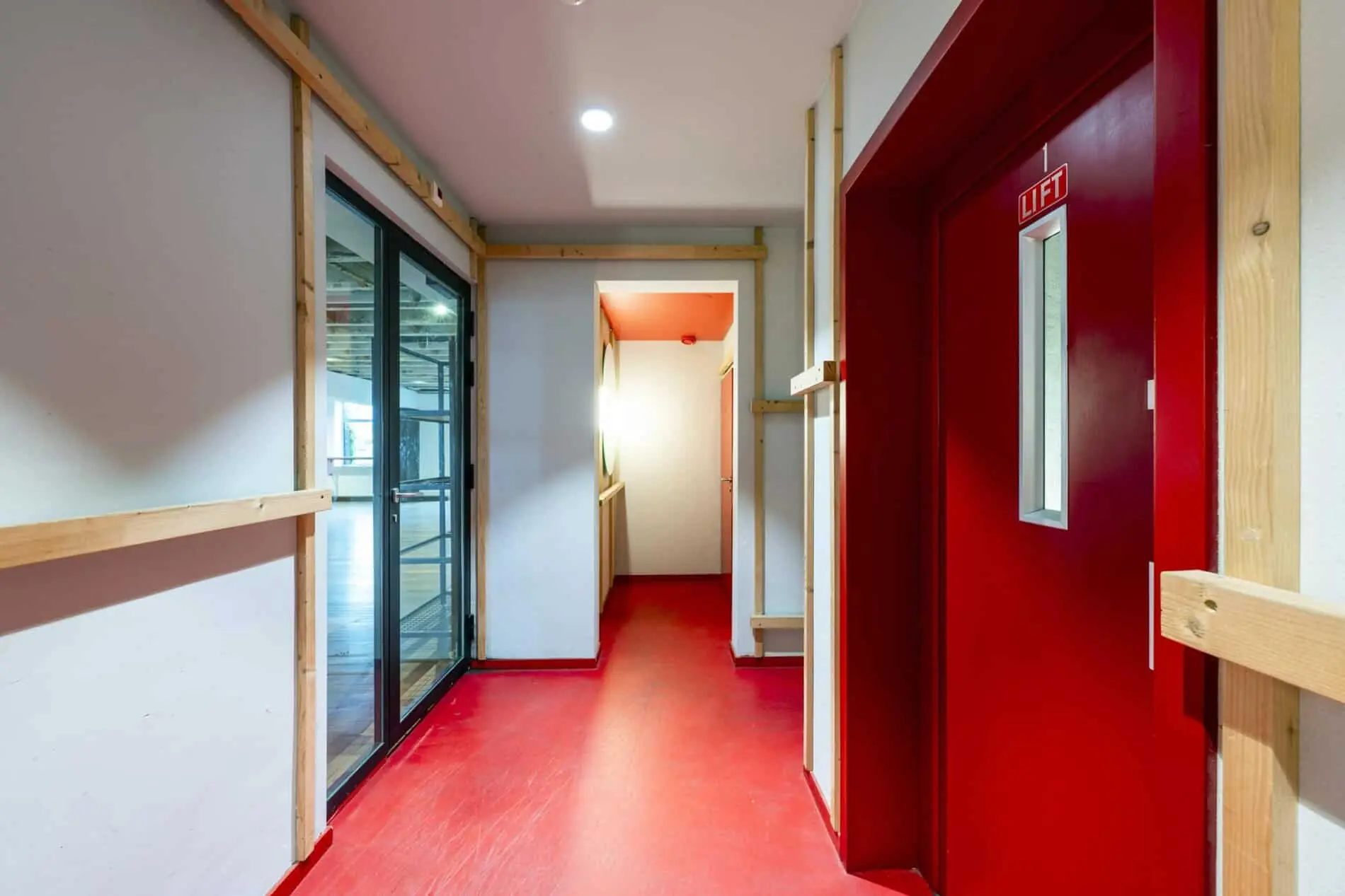 Gang met rode vloer en liftdeur in een modern kantoor aan de De Ruijterkade.