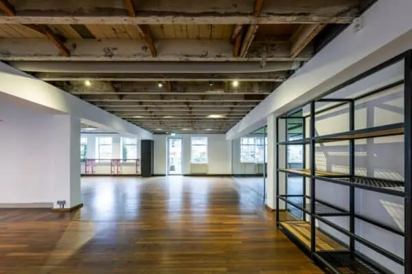 Een industriële, open kantoorruimte aan de De Ruijterkade met houten vloer, zichtbaar balkenplafond en grote ramen.