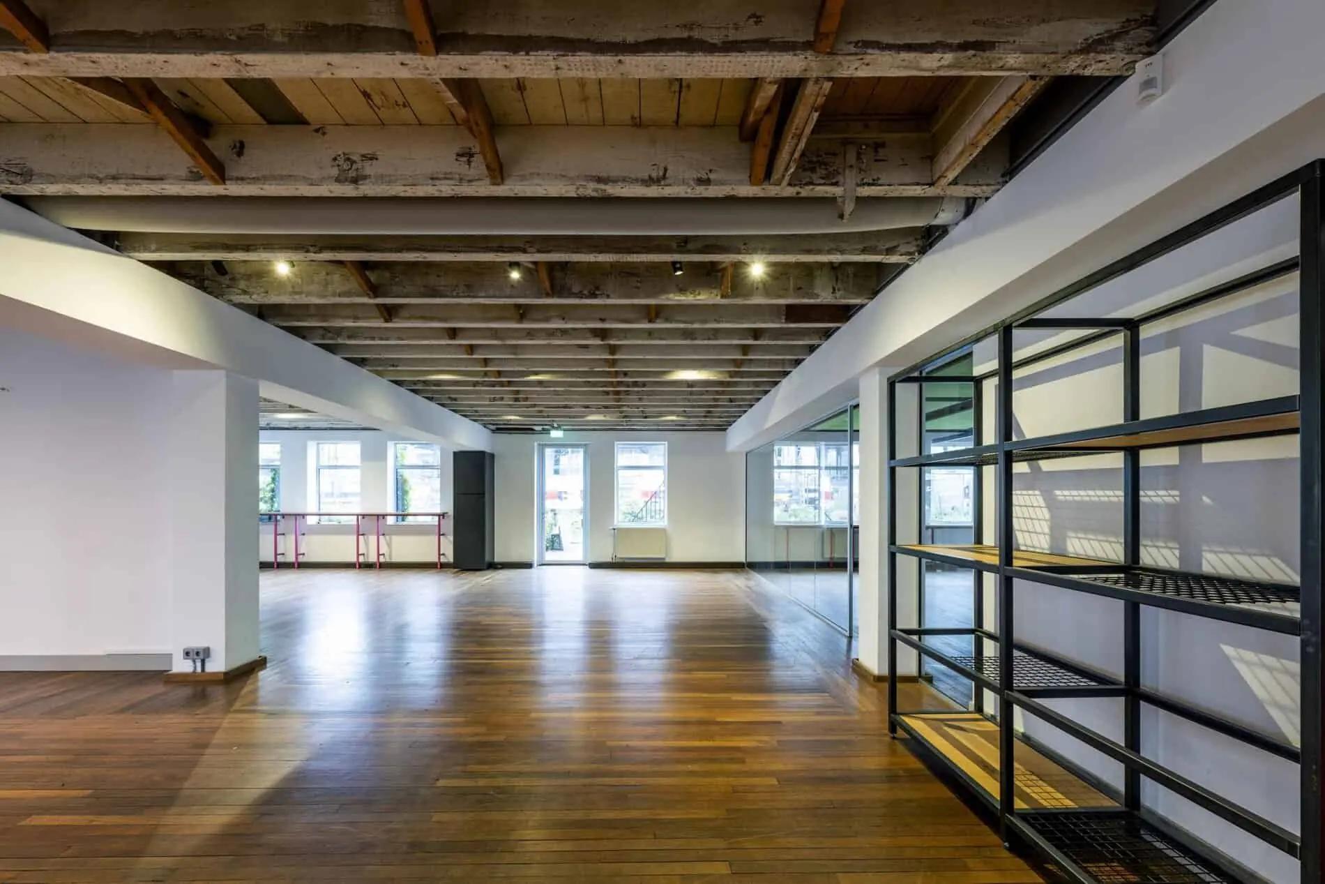 Een industriële, open kantoorruimte aan de De Ruijterkade met houten vloer, zichtbaar balkenplafond en grote ramen.