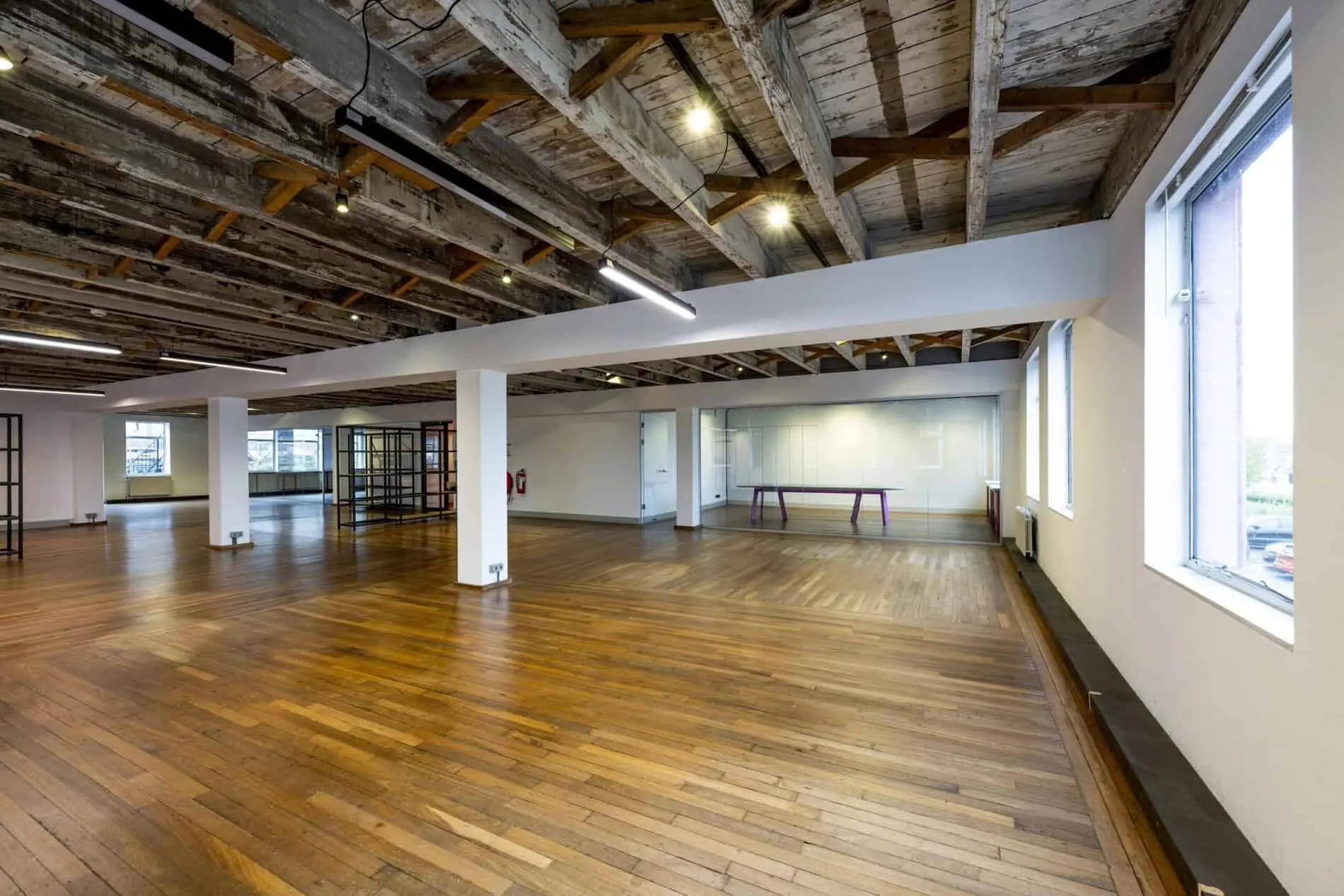 Ruime, gerenoveerde kantoorruimte aan de De Ruijterkade met houten vloer, zichtbare houten balkenplafonds en grote ramen.