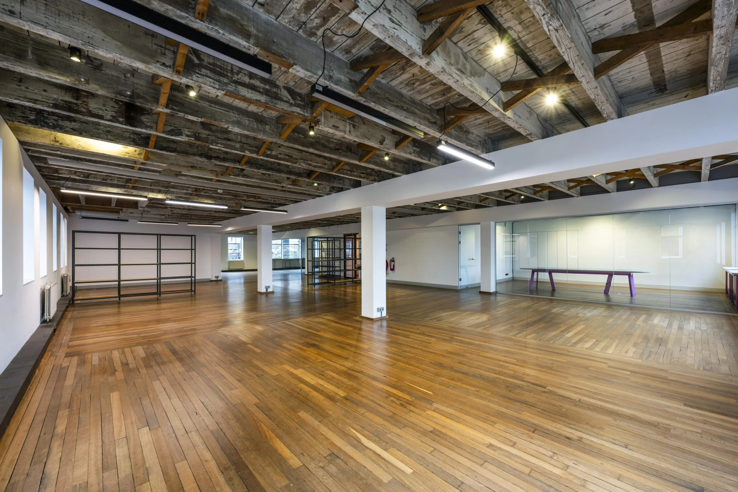 Ruim, industrieel ingericht kantoor op de De Ruijterkade met houten vloer, glazen vergaderruimte en zichtbare houten balken aan het plafond.