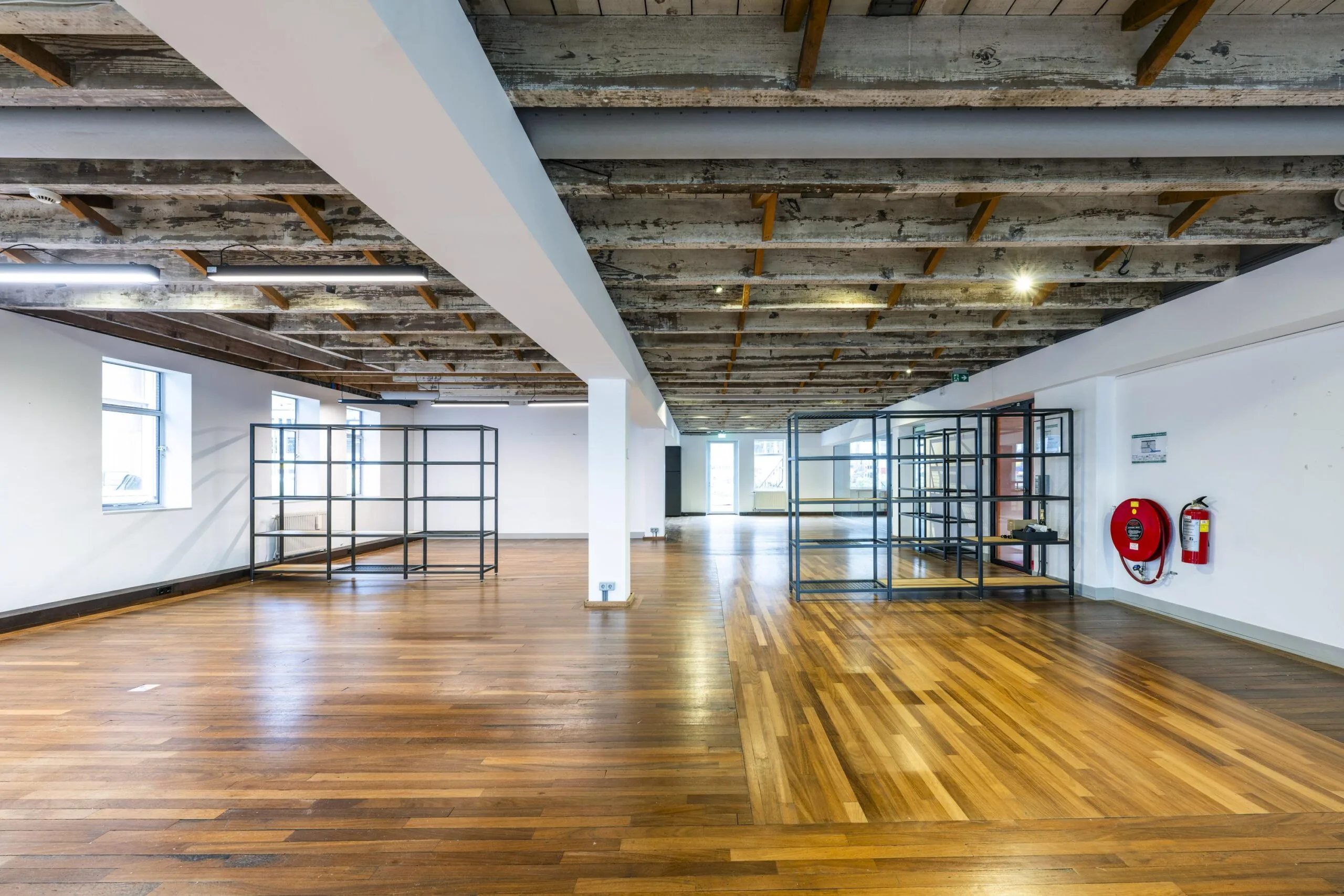 Ruime, lichte kantoorruimte aan de De Ruijterkade met houten vloer, zichtbare balkenplafonds en metalen stellingkasten.