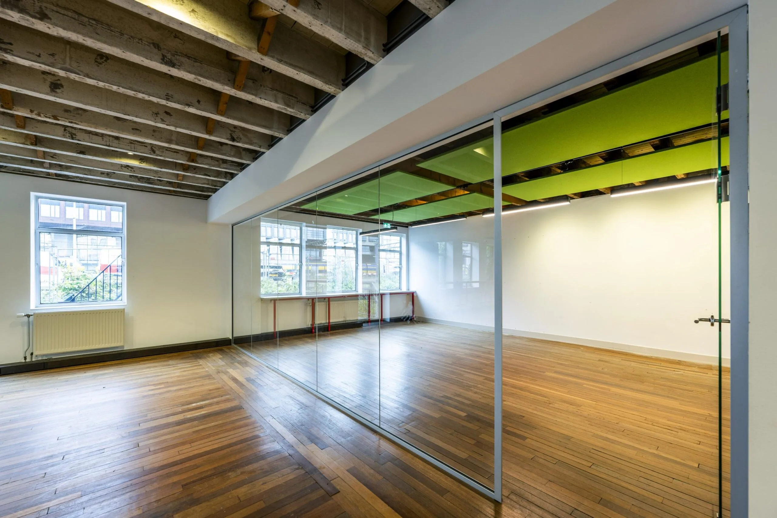 Binnenruimte aan de De Ruijterkade met houten vloer, glazen scheidingswand en zichtbare houten plafondbalken.