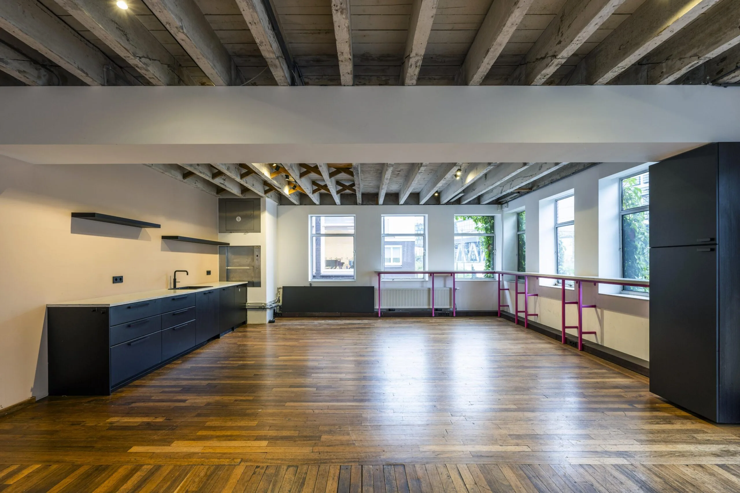 Moderne open ruimte aan de De Ruijterkade met houten vloer, zichtbare balken, zwarte keuken en grote ramen.