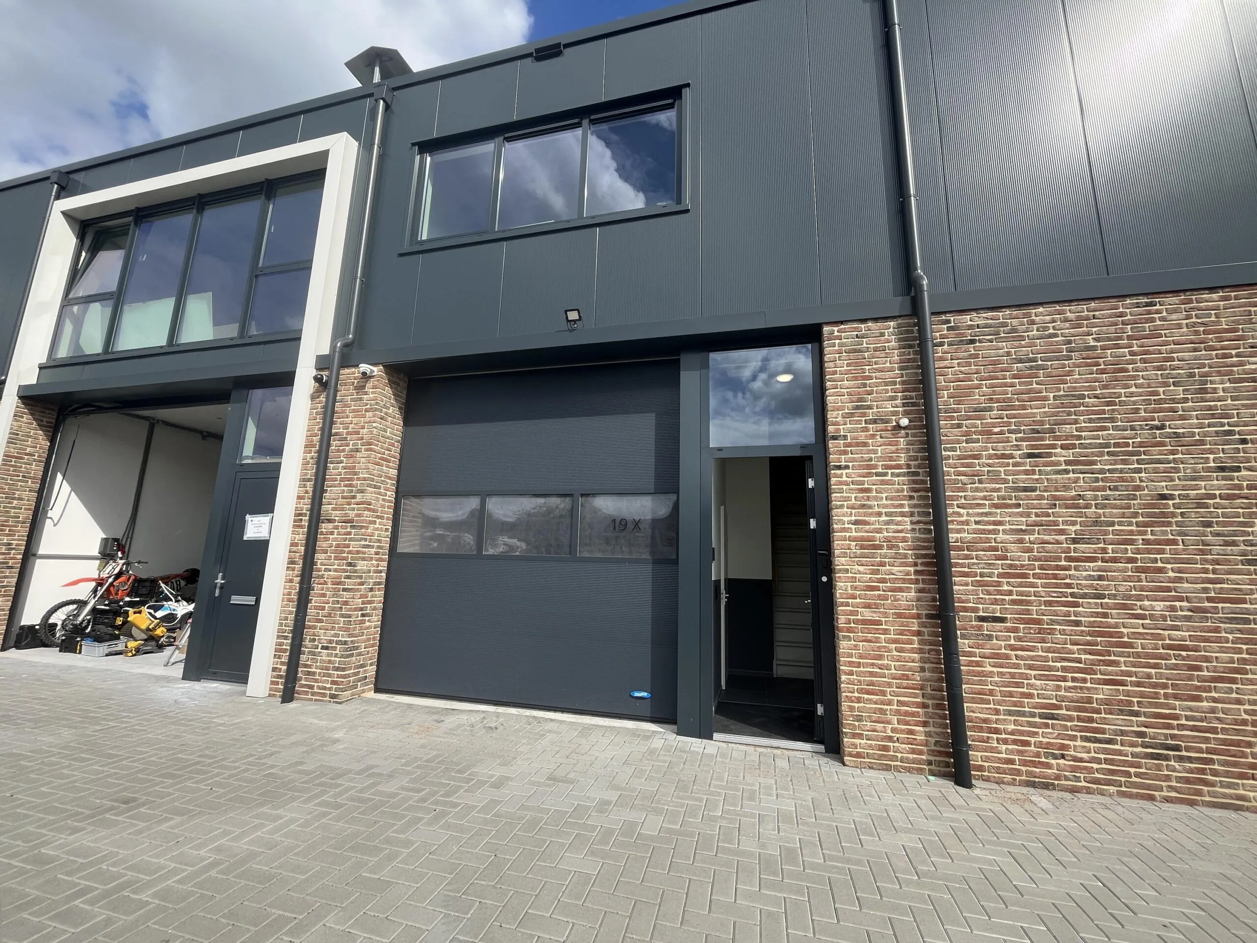 Moderne bedrijfsunit aan de Broekdijk-West met een grote zwarte roldeur, bakstenen gevel en een open toegangsdeur.
