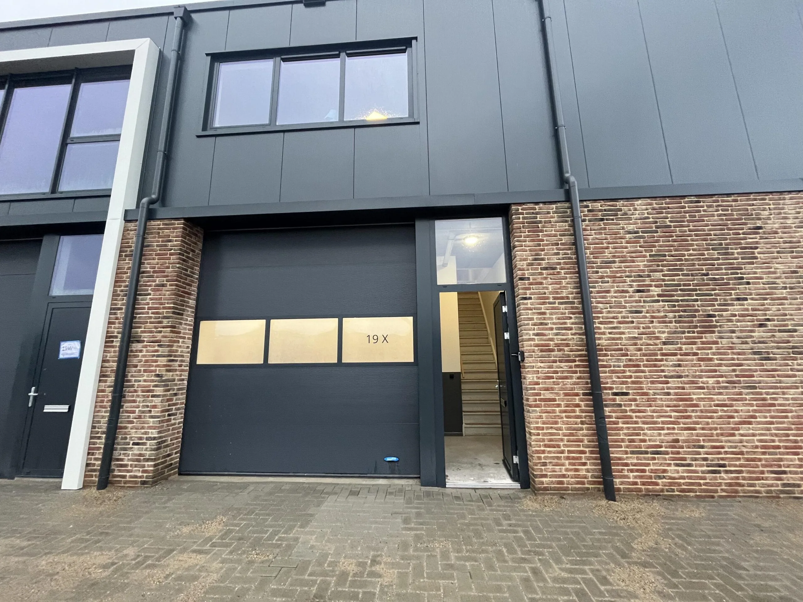 Voorgevel van bedrijfsunit 19X aan de Broekdijk West met een zwarte garagedeur, aparte ingang en bovenraam.