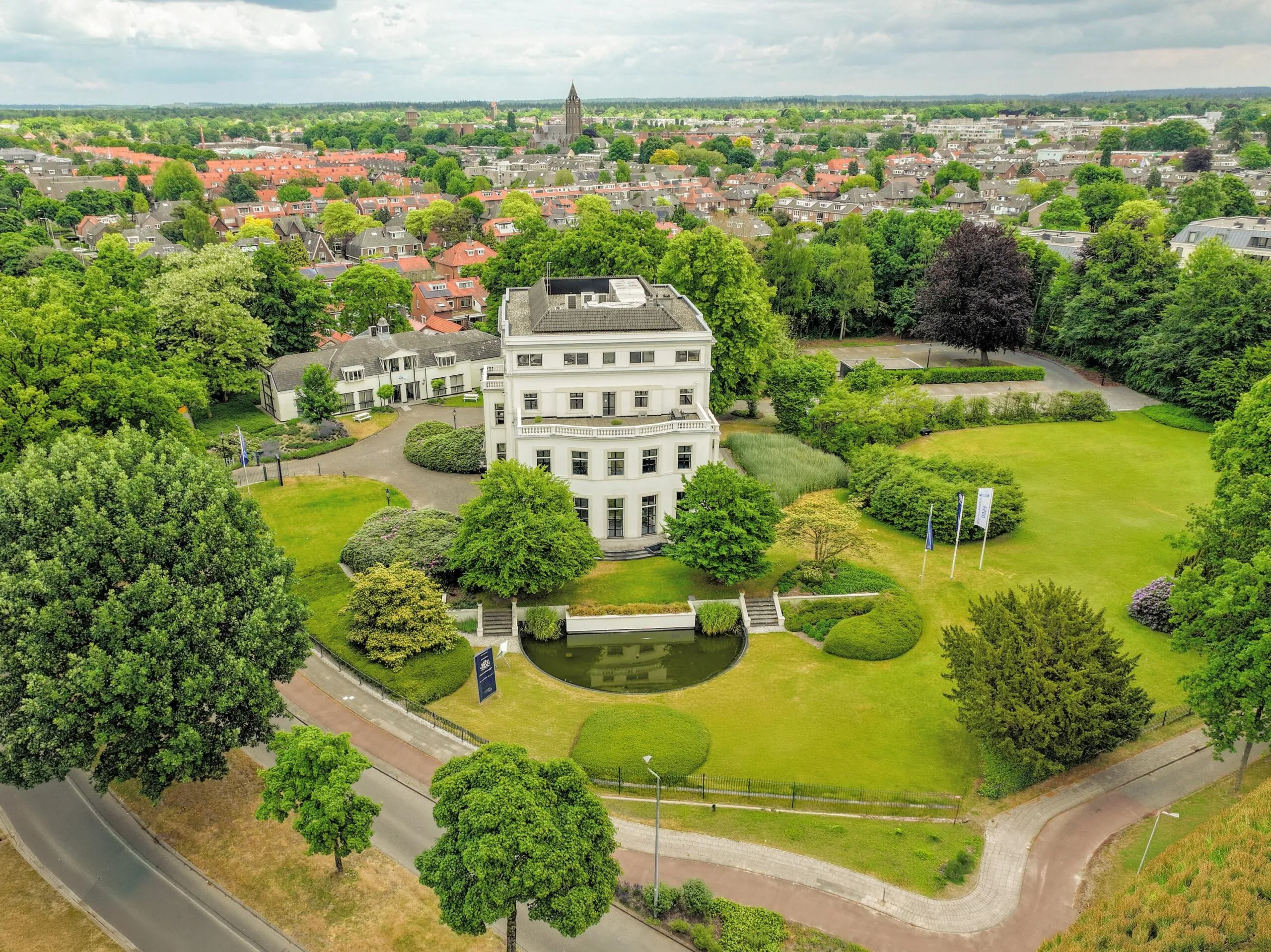 Luchtfoto van een groot wit kantoorpand aan de Utrechtseweg in een groene omgeving met uitzicht op de stad.