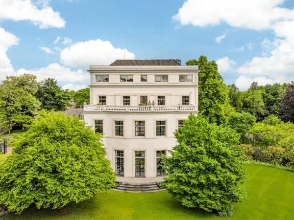 Wit herenhuis aan de Utrechtseweg omgeven door groen en bomen onder een blauwe lucht.