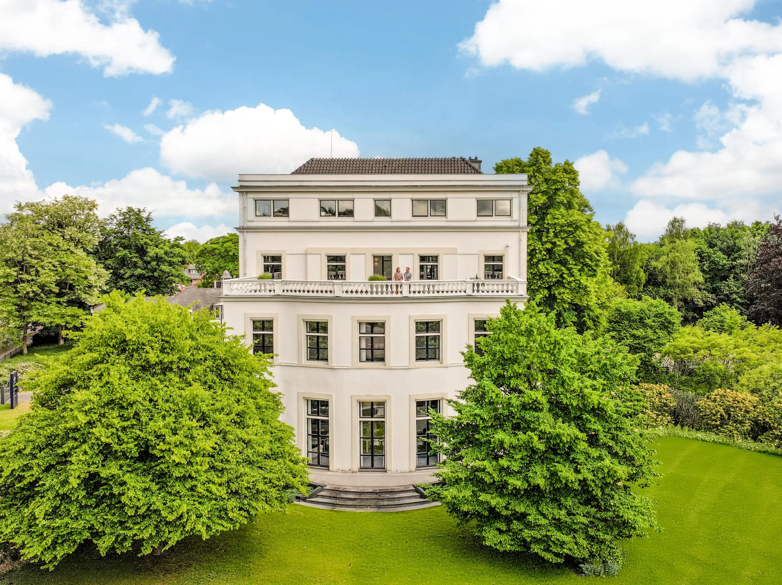 Wit herenhuis aan de Utrechtseweg omgeven door groen en bomen onder een blauwe lucht.