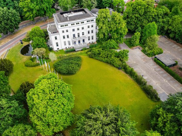 Luchtfoto van een wit herenhuis aan de Utrechtseweg, omringd door een groene tuin en parkeerterrein.