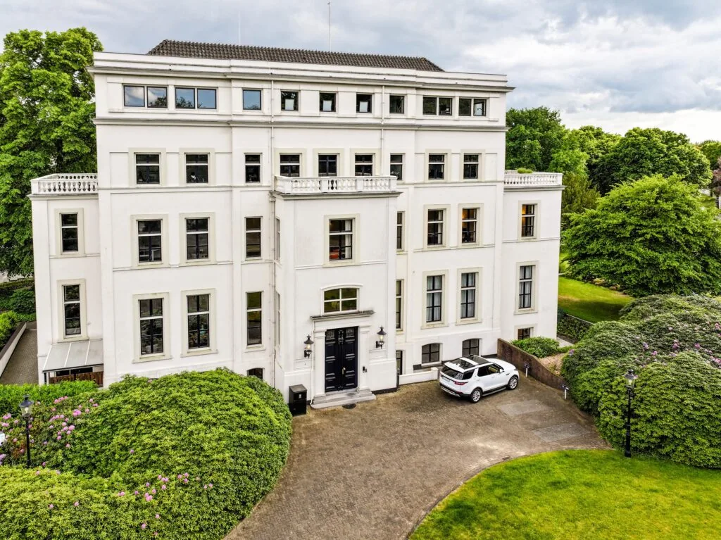 Statig wit kantoorpand aan de Utrechtseweg, omringd door groen en met een geparkeerde witte auto voor de ingang.