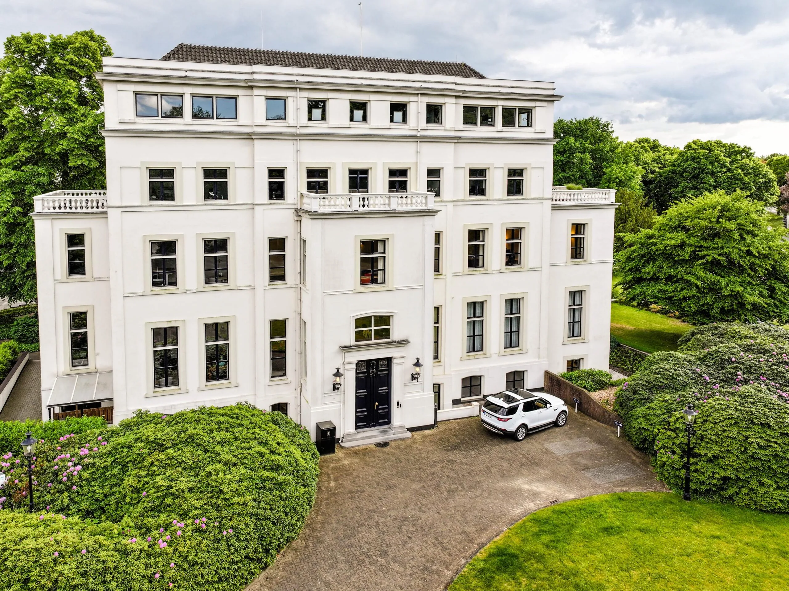 Statig wit kantoorpand aan de Utrechtseweg, omringd door groen en met een geparkeerde witte auto voor de ingang.