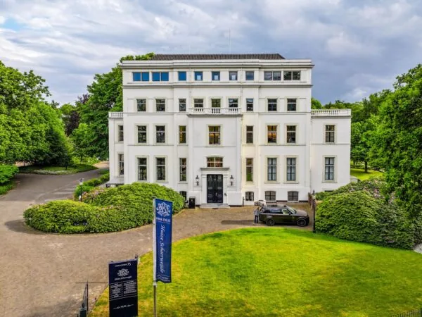 Wit herenhuis Huis Schuylenburg aan de Utrechtseweg, omgeven door groen en een oprijlaan met auto.