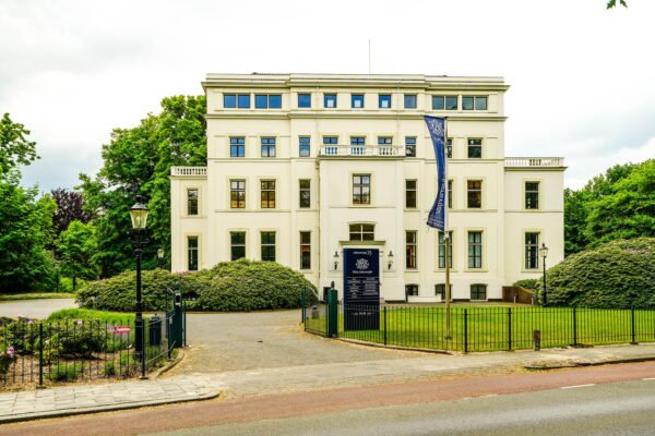 Wit herenhuis aan de Utrechtseweg 75 in Arnhem, omgeven door groen en voorzien van een toegangshek.