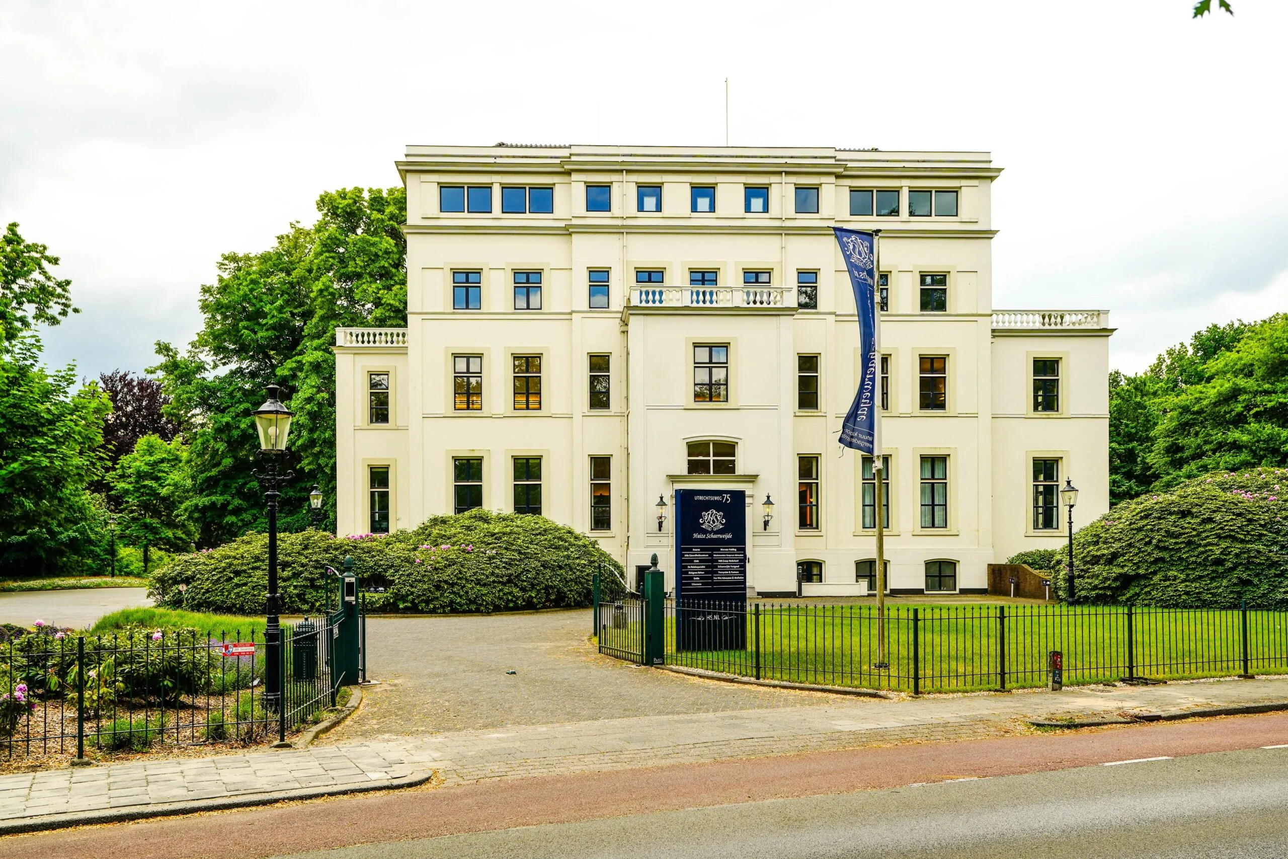 Wit herenhuis aan de Utrechtseweg 75 in Arnhem, omgeven door groen en voorzien van een toegangshek.
