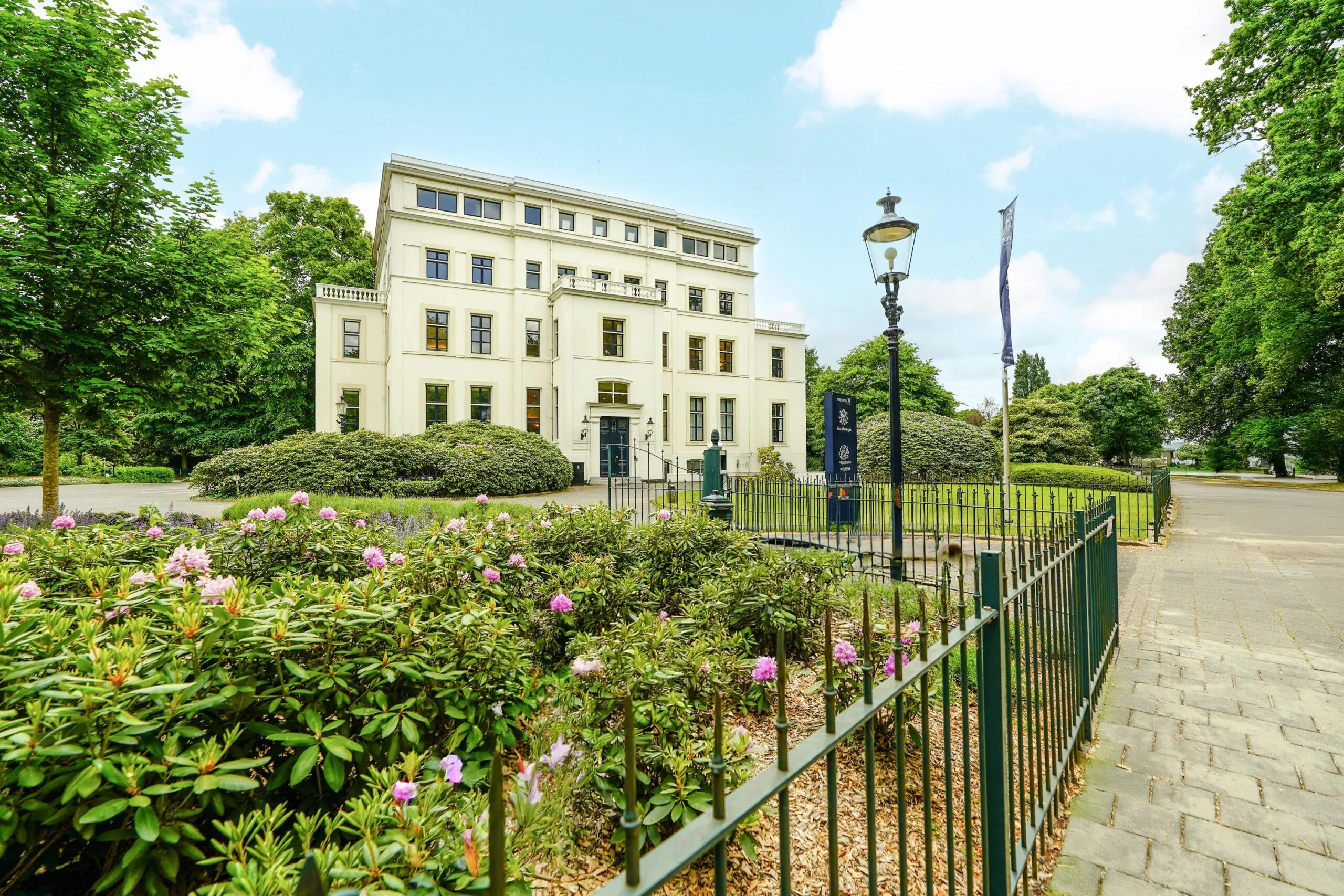 Wit klassiek kantoorpand aan de Utrechtseweg in een groene, bloemrijke omgeving.