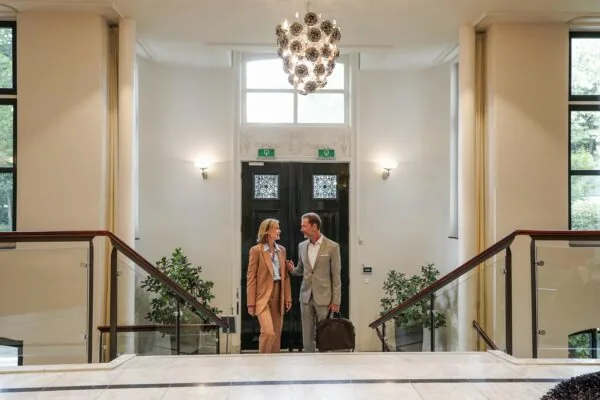 Twee zakenmensen lopen pratend een stijlvol kantoorpand aan de Utrechtseweg binnen.