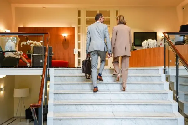 Twee zakelijk geklede personen lopen een marmeren trap op in een modern kantoorpand aan de Utrechtseweg.