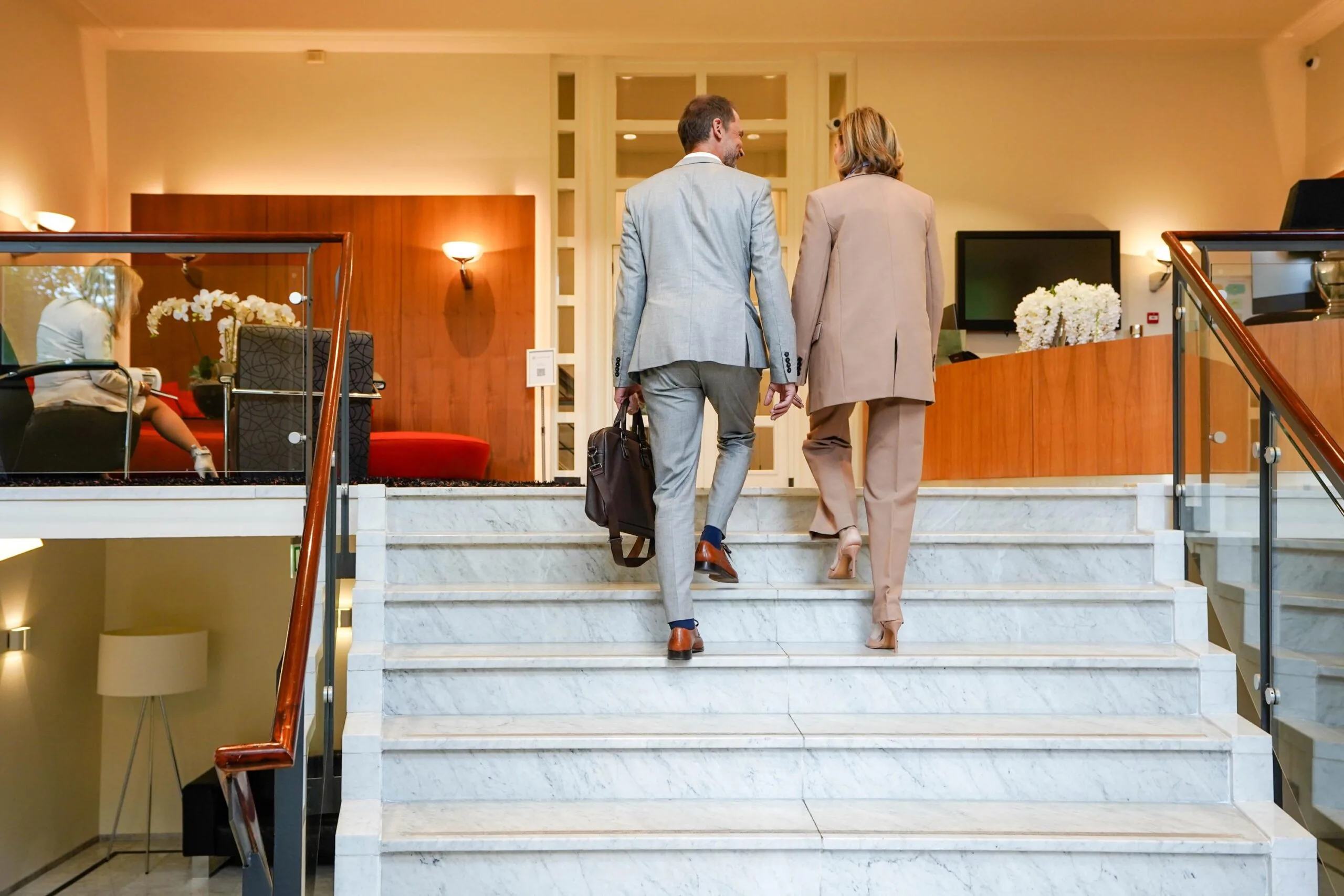 Twee zakelijk geklede personen lopen een marmeren trap op in een modern kantoorpand aan de Utrechtseweg.