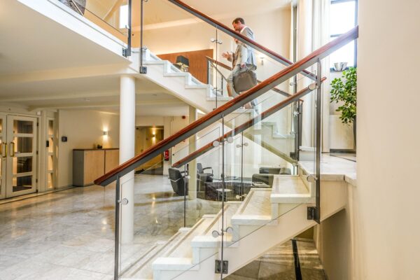 Man in pak loopt met aktetas een moderne trap af in een licht atrium aan de Utrechtseweg.