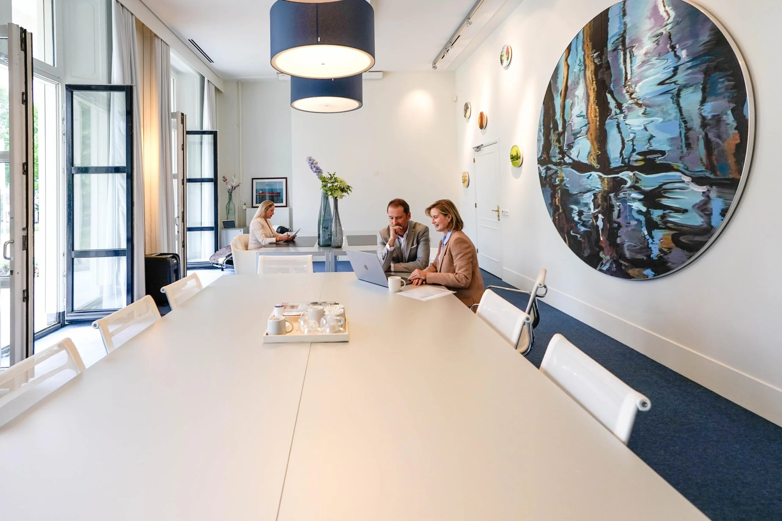 Moderne vergaderruimte aan de Utrechtseweg met grote kunstwerken aan de muur en mensen werkend aan een tafel.