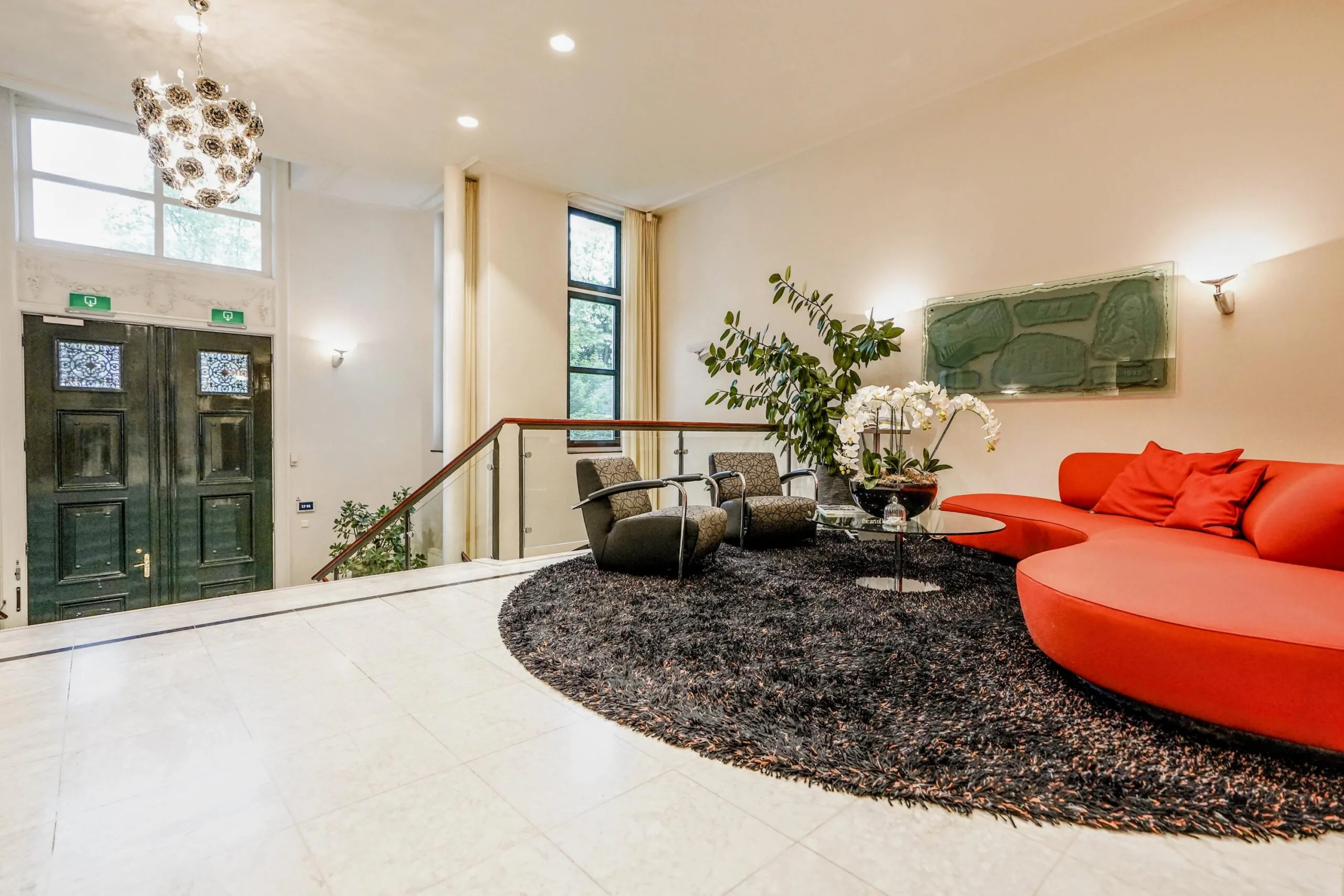 Moderne ontvangstruimte aan de Utrechtseweg met een rode designbank, zwarte fauteuils en een grote donkere vloerkleed op een lichte marmeren vloer.