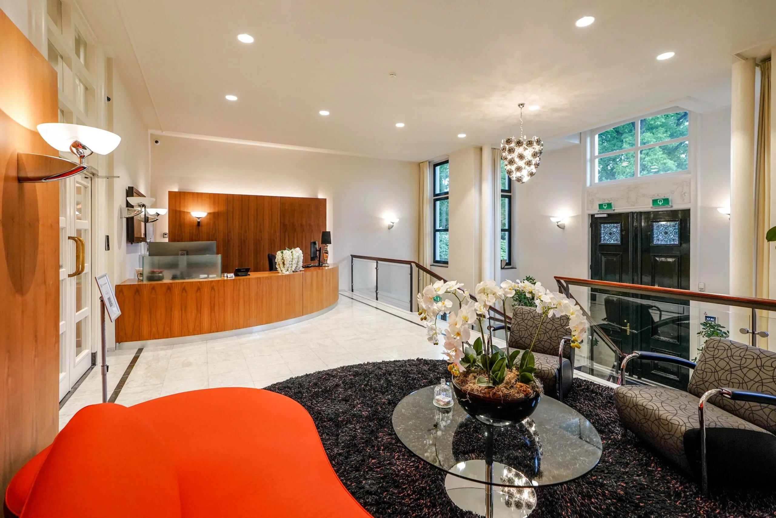 Moderne ontvangsthal aan de Utrechtseweg met houten receptiebalie, designmeubilair en glazen tafel met orchideeën.