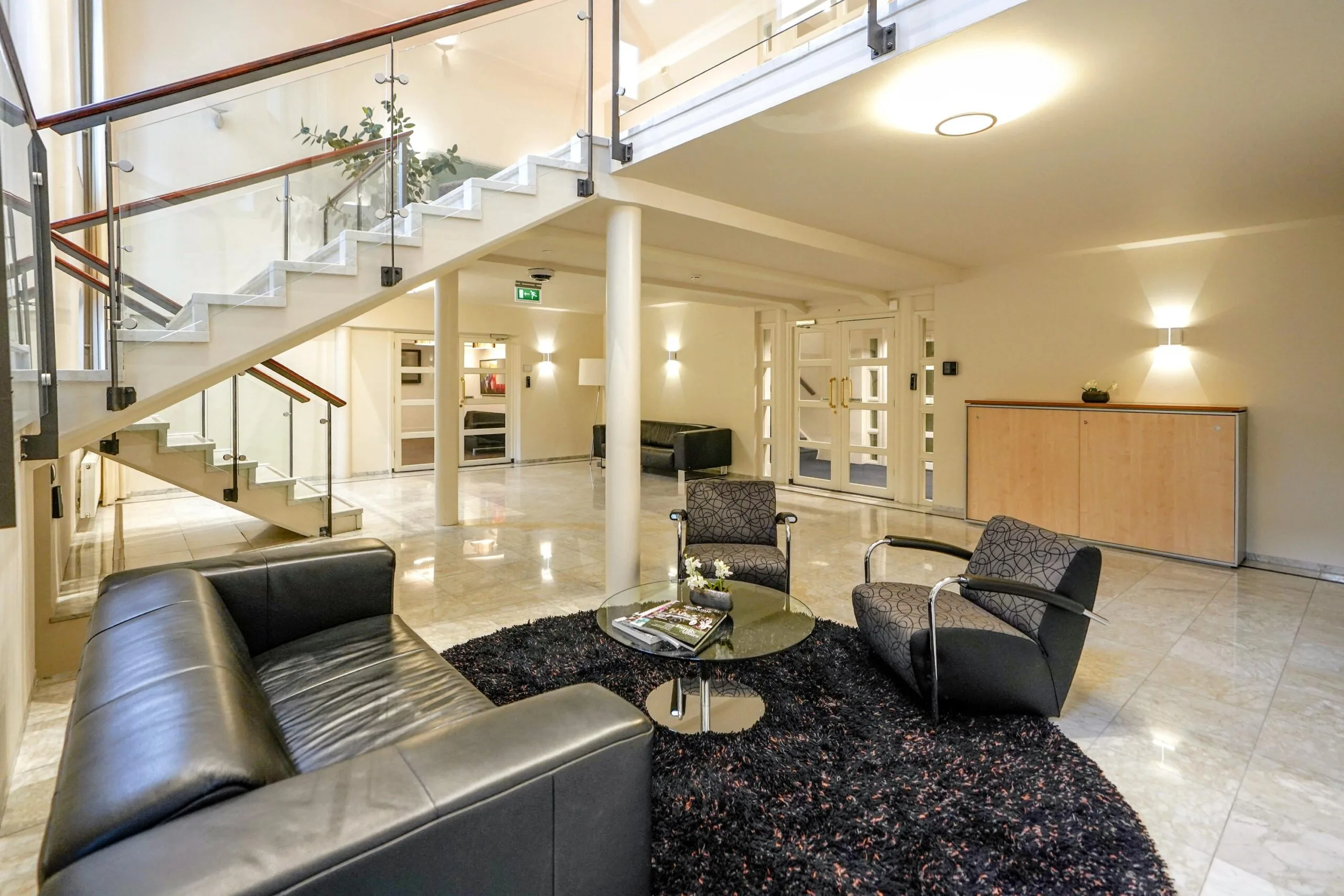 Moderne ontvangstruimte aan de Utrechtseweg met glazen trap, zitgedeelte en marmeren vloer.