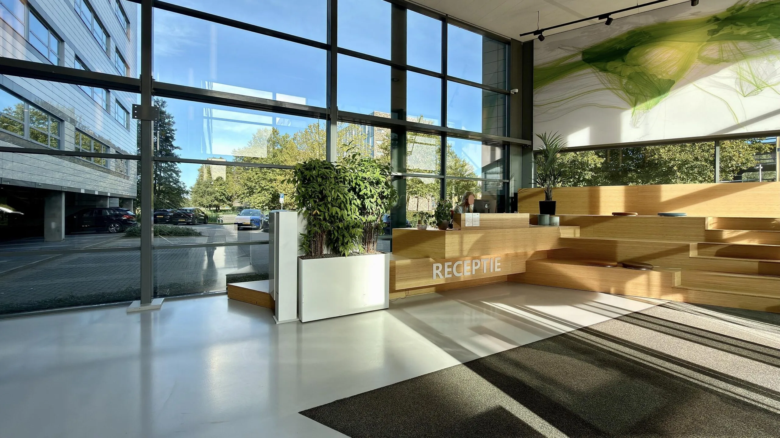 Moderne lichte ontvangsthal met houten receptiebalie en grote raampartijen aan de Papendorpseweg.