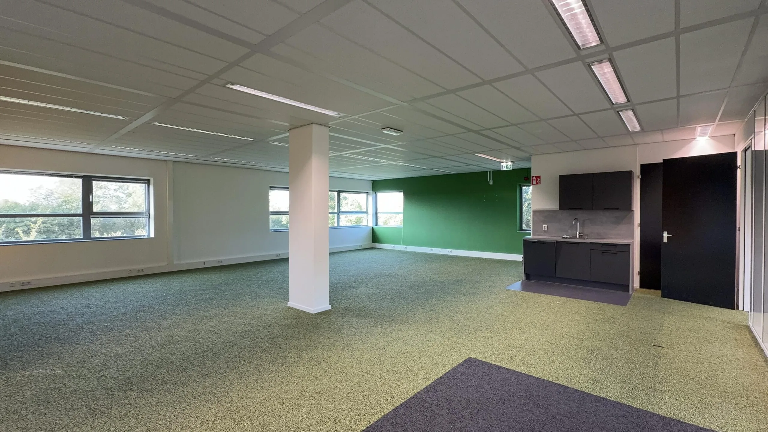 Leeg kantoorpand aan de Papendorpseweg met groene vloerbedekking, een keukenblok en grote ramen.