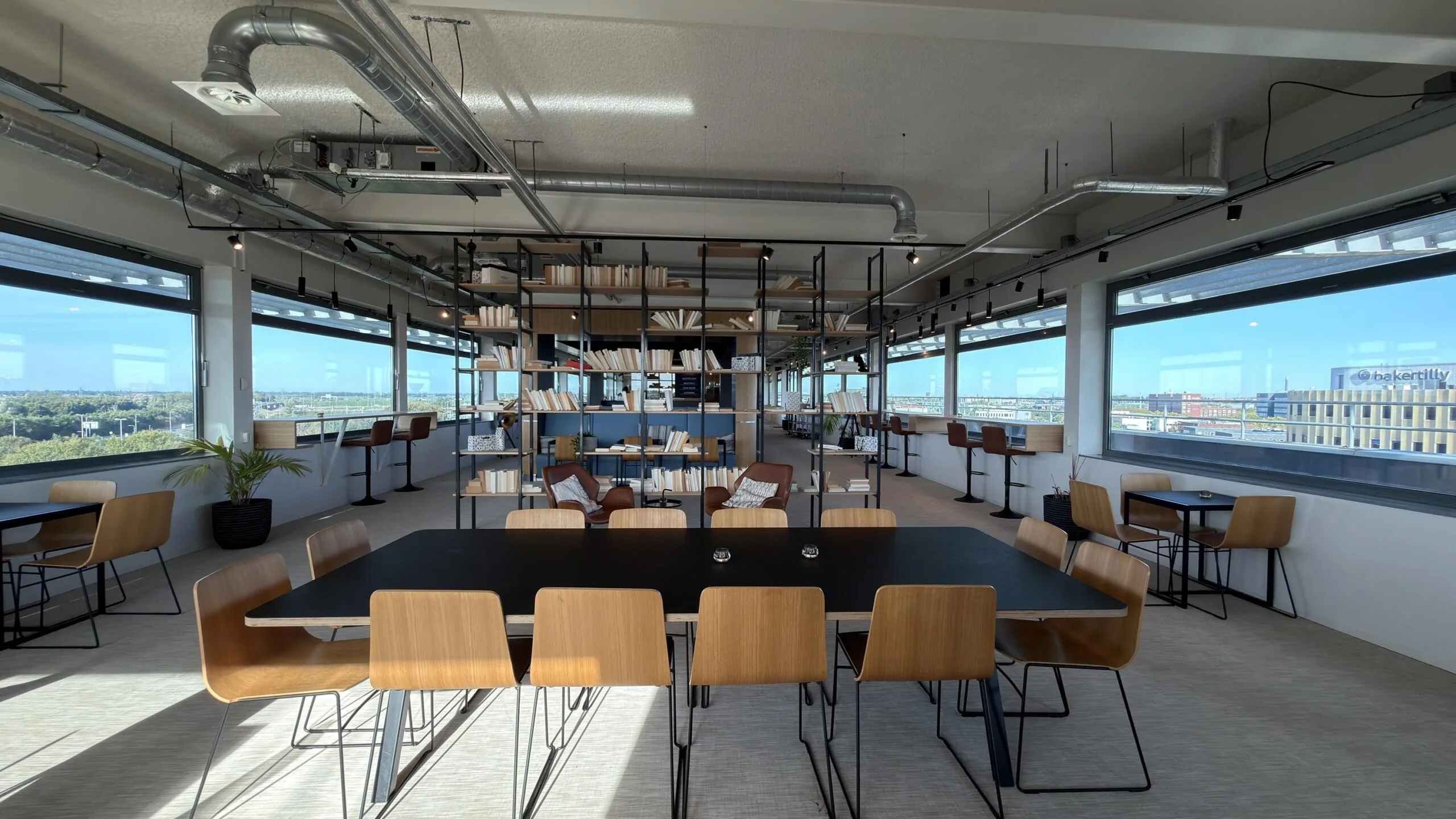Moderne en lichte kantoorlounge aan de Papendorpseweg met zitruimte, boekenplanken en uitzicht op het Baker Tilly-gebouw.