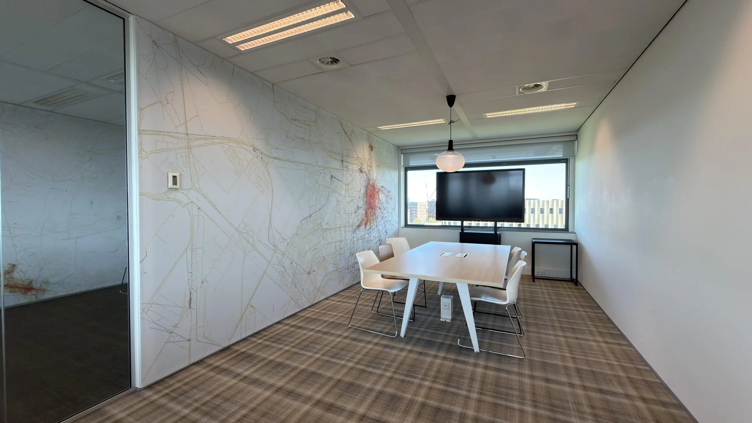 Vergaderruimte in een modern kantoorpand aan de Papendorpseweg met muurdecoratie in de vorm van een plattegrond, een vergadertafel, vier stoelen en een groot presentatiescherm.
