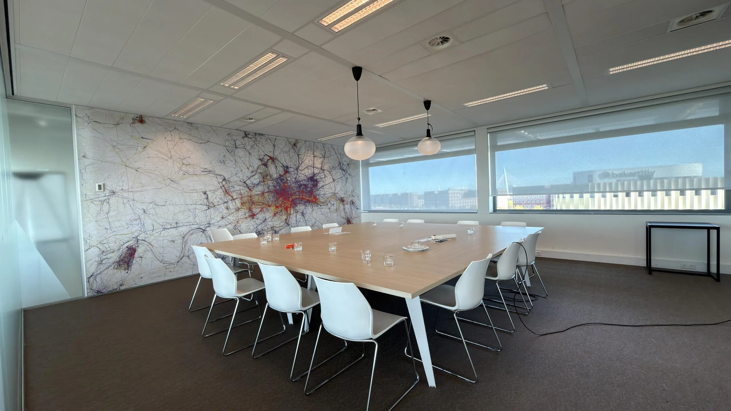 Vergaderruimte met grote houten tafel, witte stoelen, een kleurrijke kaart op de muur en uitzicht op het Bakertilly-gebouw aan de Papendorpseweg.