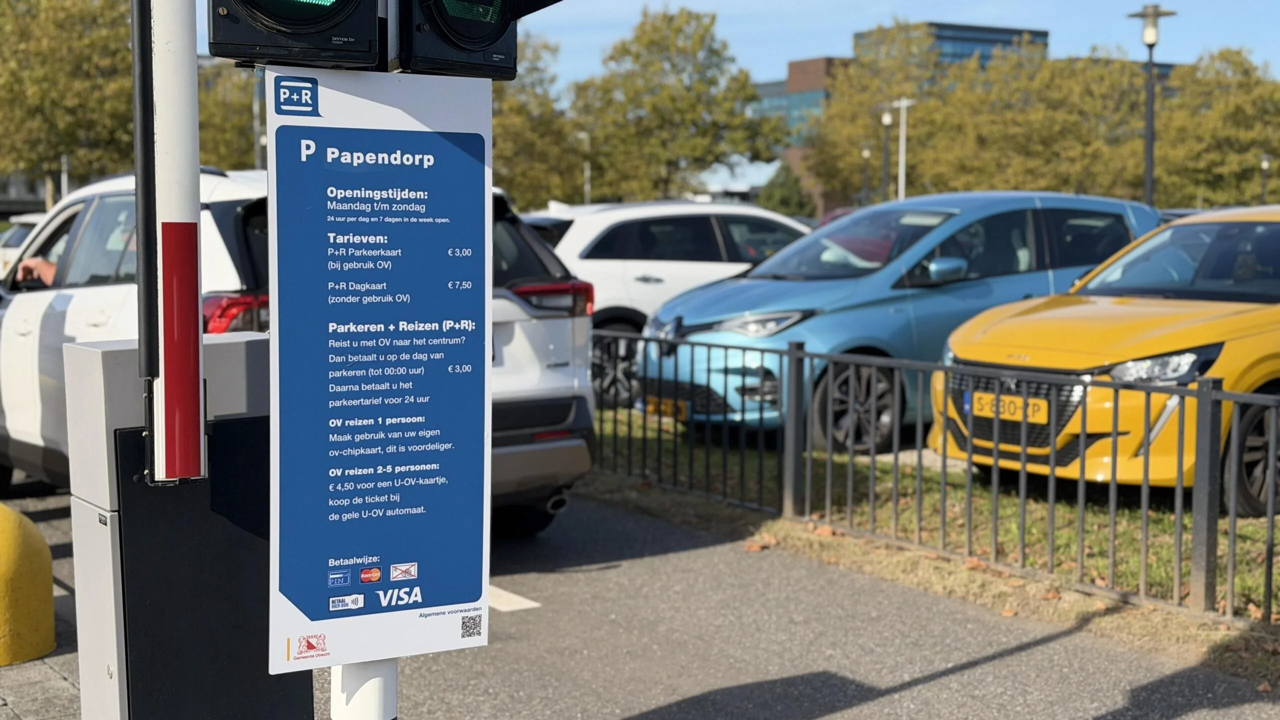 Informatiebord bij P+R Papendorp met parkeertarieven en voorwaarden, met auto's op de achtergrond.