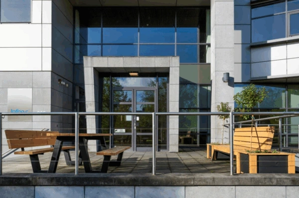 Ingang van een modern kantoorpand aan de Boeing Avenue met houten zitbanken en planten op het terras.