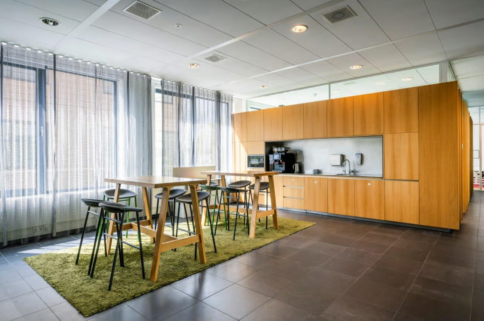 Moderne pantry met houten keukenkasten, hoge tafels, barkrukken en grote ramen met lichte gordijnen in een kantoor aan de Boeing Avenue.