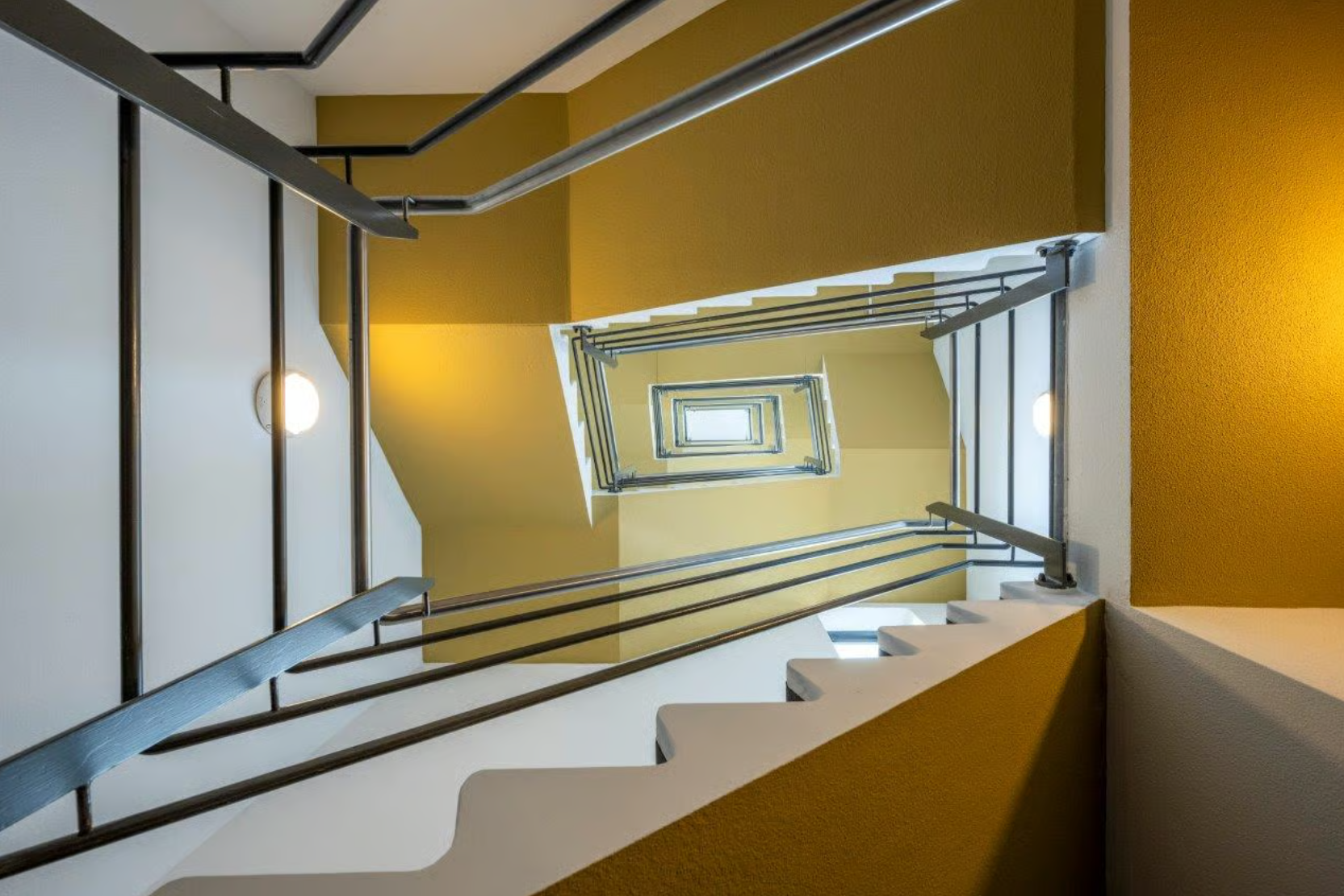 Blik omhoog in een trappenhuis aan de Boeing Avenue met geel-witte muren en metalen leuningen.