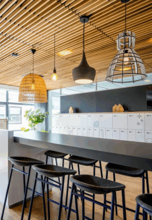 Moderne kantoorkeuken aan de Boeing Avenue met een hoge tafel, barkrukken, sfeervolle hanglampen en witte lockers op de achtergrond.