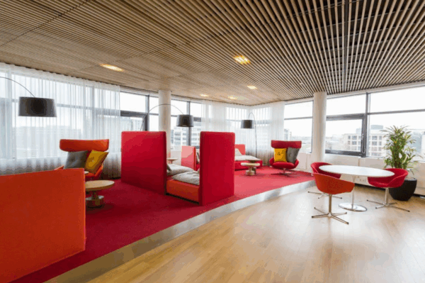 Moderne, kleurrijke lounge- en werkruimte met rood tapijt, designstoelen en grote ramen in een kantoor aan de Boeing Avenue.