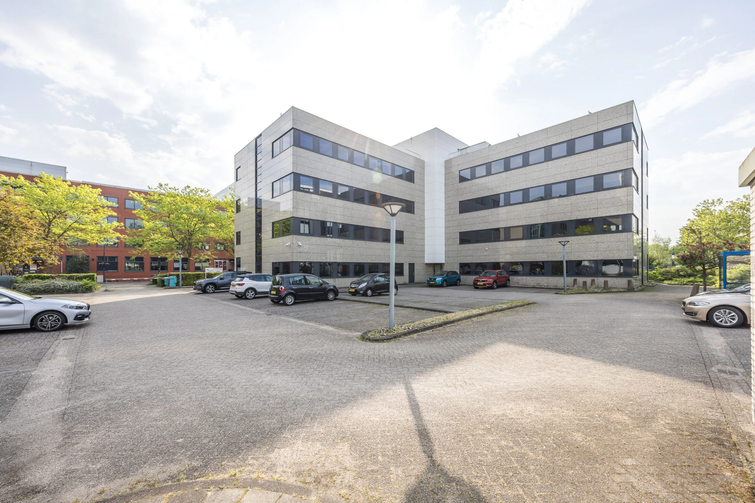 Kantoorgebouw aan de Varrolaan met parkeergelegenheid op de voorgrond op een zonnige dag.